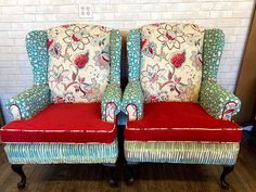 two chairs with red and blue upholstered cushions sitting side by side in front of a white brick wall