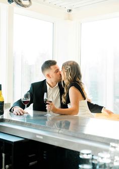 a man and woman sitting at a bar kissing with wine in front of the window