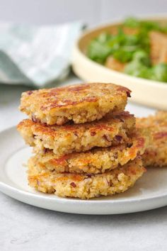 three crab cakes on a plate next to a bowl of salad