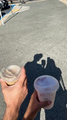 a person holding up a cup of coffee in the middle of an empty parking lot