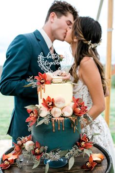 a bride and groom kissing in front of a wedding cake with flowers on the side