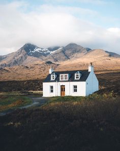 a white house sitting on top of a lush green field next to a tall mountain