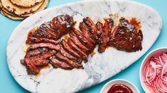 sliced steak on a marble platter with red onions and pita bread next to it