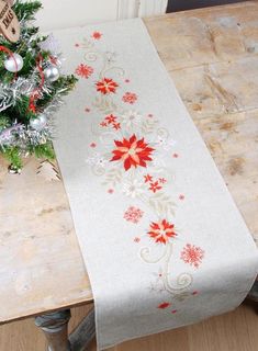 a christmas table runner with poinsettis on it and a tree in the background