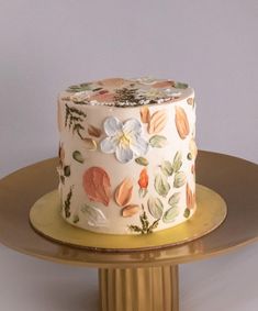 a white cake with flowers and leaves on it sitting on top of a gold plate