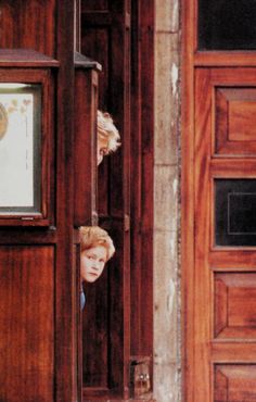 a young boy peeking out from behind a wooden door with a clock on the wall