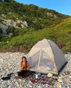 a woman sitting on the ground next to a tent