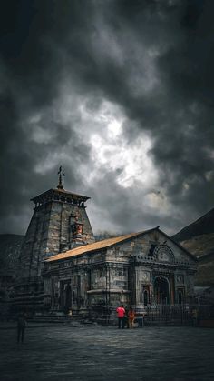 two people standing in front of a building under a cloudy sky with dark clouds above