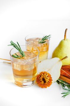 two glasses filled with liquid next to pears and cinnamon sticks on a white surface