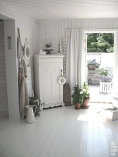 a living room with white walls and wood flooring is pictured in this image, there are potted plants on the far side of the window sill