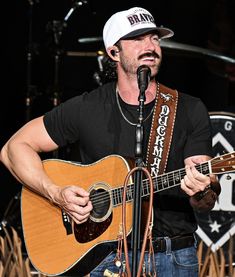 a man holding a guitar while standing in front of a microphone and wearing a bandana