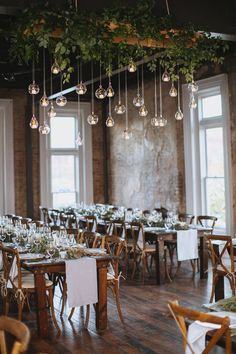 the tables are set up for an event with hanging chandeliers and greenery