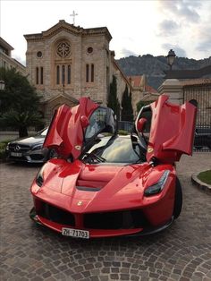 a red sports car is parked in front of a church with its doors open and it's hood up