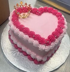 a heart shaped cake with pink frosting and a gold crown on top is sitting on a silver platter