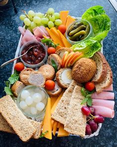 a platter filled with meats, cheeses, fruit and crackers on top of a table