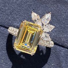 a yellow diamond ring sitting on top of a black stone surface with diamonds around it