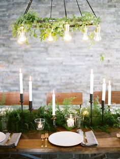 the table is set with white plates and silverware, candles, and greenery