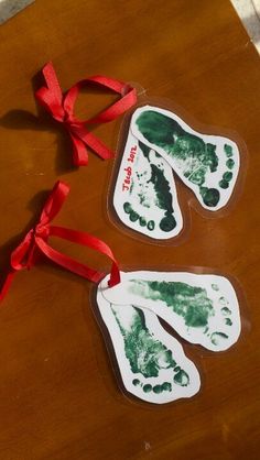 two hand and foot prints are tied to red ribbon on a wooden table with a pair of scissors