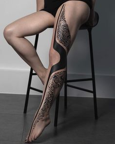 a woman is sitting on a chair with her legs covered in black and white tattoos