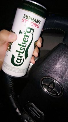 a person holding a can of coffee in their hand while sitting in a car with the steering wheel behind them