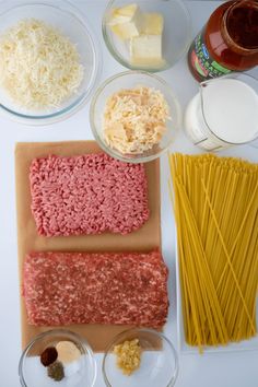 ingredients to make pasta laid out on a cutting board, including ground meat, cheese and noodles