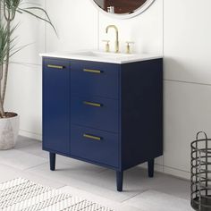 a bathroom vanity with blue drawers and a round mirror on the wall next to a potted plant