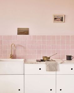 a kitchen with pink tiles on the wall and white cupboards in front of it