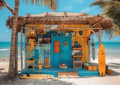 a blue and yellow hut on the beach with surfboards