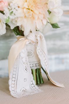 a bouquet of white and pink flowers in a glass vase with lace on the side