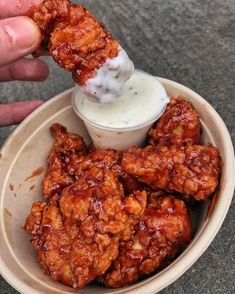 a person dipping something into a bowl with chicken wings in it and ranch dressing on the side