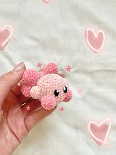 a hand holding a pink stuffed animal with hearts on it's back and eyes