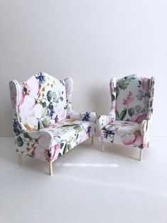 two chairs with floral upholstered cushions are sitting side by side in front of a white wall