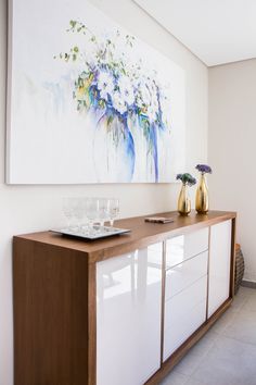 a painting hanging on the wall next to a buffet table with wine glasses and vases