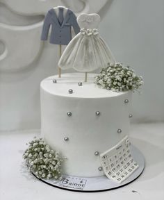 a white wedding cake with a dress and jacket on top is decorated with baby's breath flowers