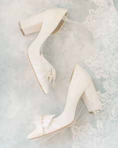 two pairs of white high heeled shoes with bows on the toes and lace detailing