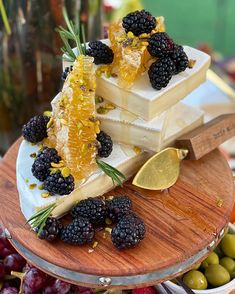 three slices of cheese with blackberries and honey on a wooden platter next to olives