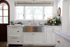 a kitchen with white cabinets and gold trim on the windowsill is decorated with flowers