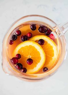 two orange slices and cranberries in a glass mug filled with liquid on a white surface