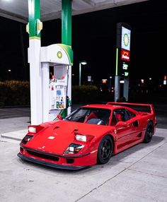 a red sports car parked in front of a gas station pump at night with its lights on