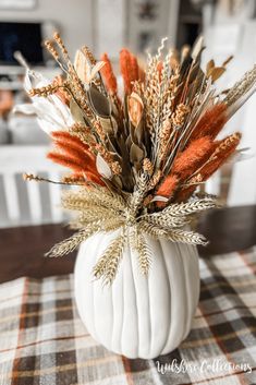 a white pumpkin filled with dried plants on top of a plaid tablecloth covered table