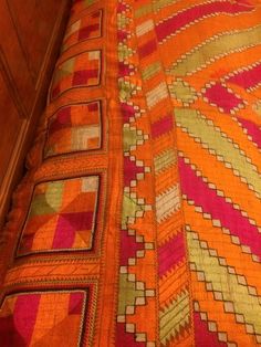 an orange and pink quilt is laying on a bed