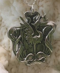 a silver necklace with an ornate design on the front and back of it, sitting on a white furnishing