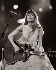 a woman holding a guitar while standing in front of a microphone