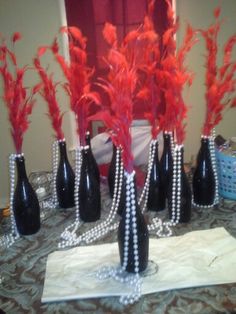 several black vases with red flowers and pearls on the table cloth in front of a mirror