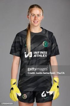 a female soccer player poses for a photo in black and white uniform with yellow gloves