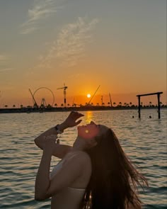 a woman is standing in the water at sunset with her eyes closed and hands up to her face