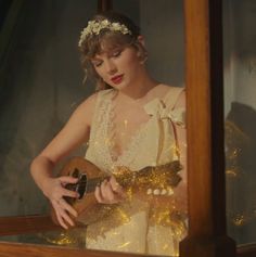 a woman in a white dress is holding a guitar and looking at herself through a mirror