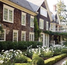 a large brown house with white flowers in the front yard and bushes on either side