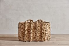 a large woven basket sitting on top of a wooden floor next to a white wall