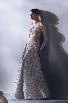 Honey Waqar Bridal Lehenga Choli and Dupatta Dress is a stunning attire adorned with lavish designs and hand-crafted embellishments. Premium organza fabric and shimmering ornaments give a glamorous touch to this perfectly stitched Pakistani Bridal Dress. Lehenga Choli: The choli in an alluring grey color is intricately emblazoned with zardosi, embroidery, and motifs. Intricate designs and fine details of silverwork give a perfect finishing look to the choli. Moreover, the stylish neckline and ha Designer Embellished Silver Lehenga, Designer Embellished Silver Choli, Silver Embellished Choli For Festivals, Embellished Silver Choli For Festivals, Designer Silver Embellished Choli, Traditional Silver Designer Dresses, Silver Anarkali Style Hand Embellished Sharara, Traditional Silver Festive Dress, Fitted Silver Hand Embellished Lehenga